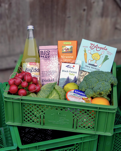 KI generiert: Eine grüne Kiste mit Bio-Produkten: Radieschen, Getränke, Getreide, Tofu, Nudeln, Brokkoli, Obst und mehr.