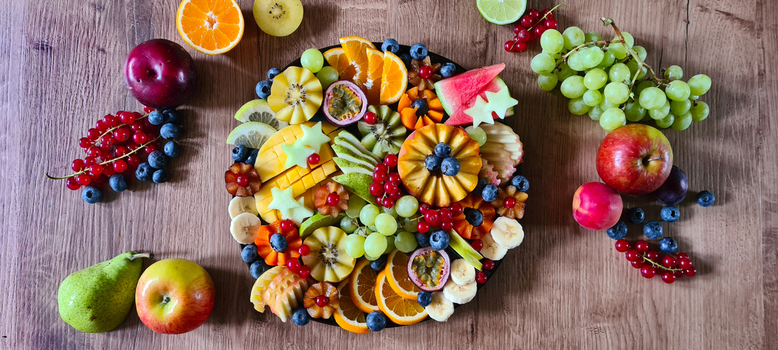 KI generiert: Bunte Obstplatte mit verschiedenen geschnittenen Früchten und Beeren auf einem Holztisch arrangiert.