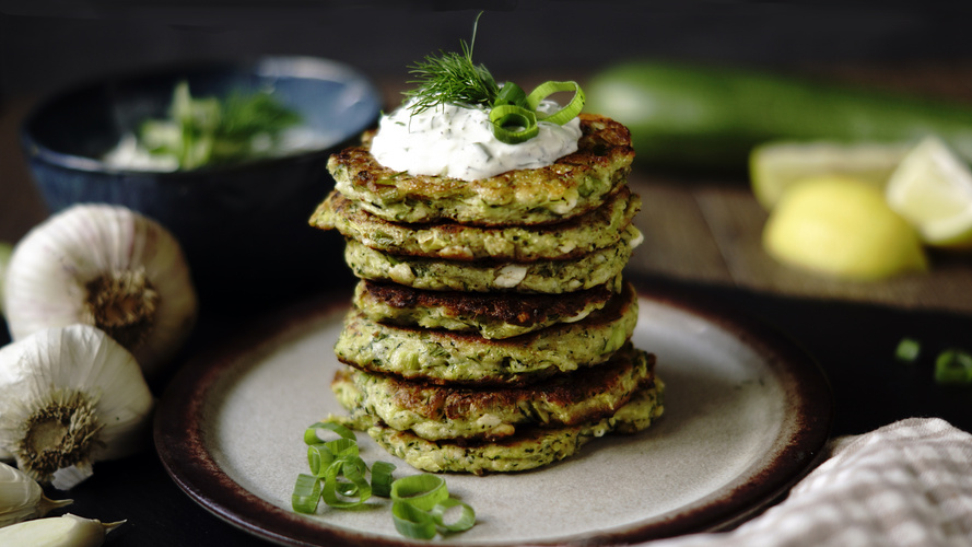KI generiert: Ein Stapel Zucchinipuffer mit Kräuterquark, dekoriert mit Dill und Frühlingszwiebeln auf einem Teller.