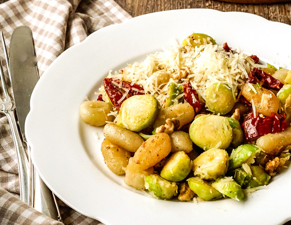 KI generiert: Das Bild zeigt eine Pfanne mit gefüllten, aufgerollten Zucchinischeiben in einer Tomatensauce, dekoriert mit Frühlingszwiebeln. Im Hintergrund sind Gewürzschalen zu sehen.