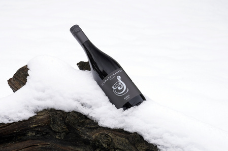 KI generiert: Das Bild zeigt eine Weinflasche mit der Aufschrift "Schönhals Samt & Seide" auf einer hölzernen Treppe, die von einem grauen Stoff umgeben ist. Der Fokus liegt auf der Weinflasche.