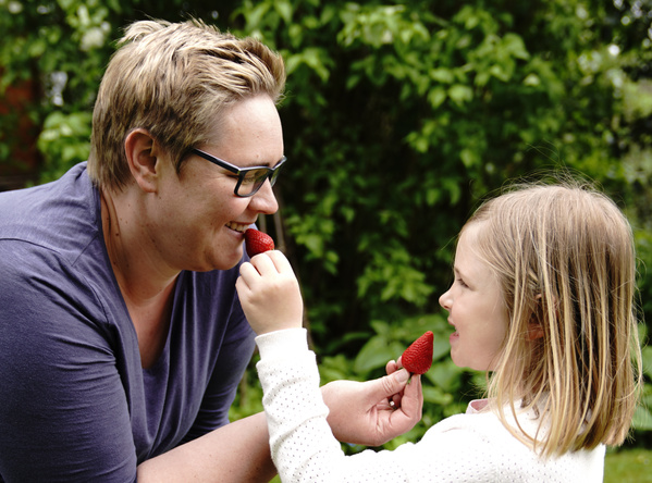 KI generiert: Zwei Personen stehen in einem Gewächshaus voller Pflanzen und halten eine Kiste mit frischem Gemüse. Der Fokus liegt auf der Präsentation der Ernte.