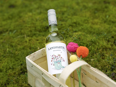 KI generiert: Das Bild zeigt eine Weinflasche mit der Aufschrift "Schönhals Samt & Seide" auf einer hölzernen Treppe, die von einem grauen Stoff umgeben ist. Der Fokus liegt auf der Weinflasche.