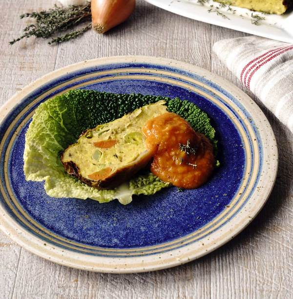 KI generiert: Ein Gemüsekuchen und Sauce auf einem blauen Teller, dekoriert mit Kohlblatt.