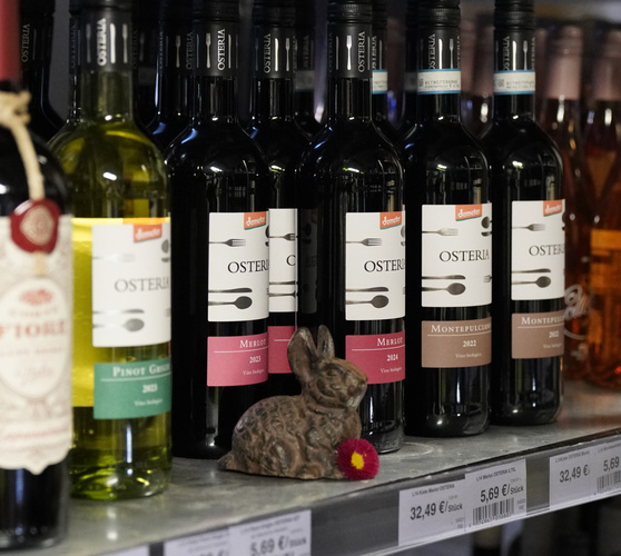 KI generiert: Weinflaschen von "Osteria" im Regal, daneben eine Häschenfigur. Preisschilder: 5,69 € pro Stück, 32,49 € pro Karton.