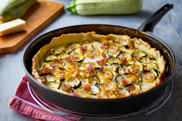 KI generiert: Zucchini-Quiche in einer Pfanne, umgeben von Zucchini und Käse auf einem Schneidebrett.