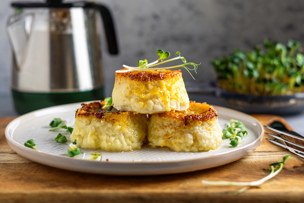 KI generiert: Drei goldbraune Röstitaler auf einem Teller, garniert mit Kräutern, im Vordergrund einer Teekanne.