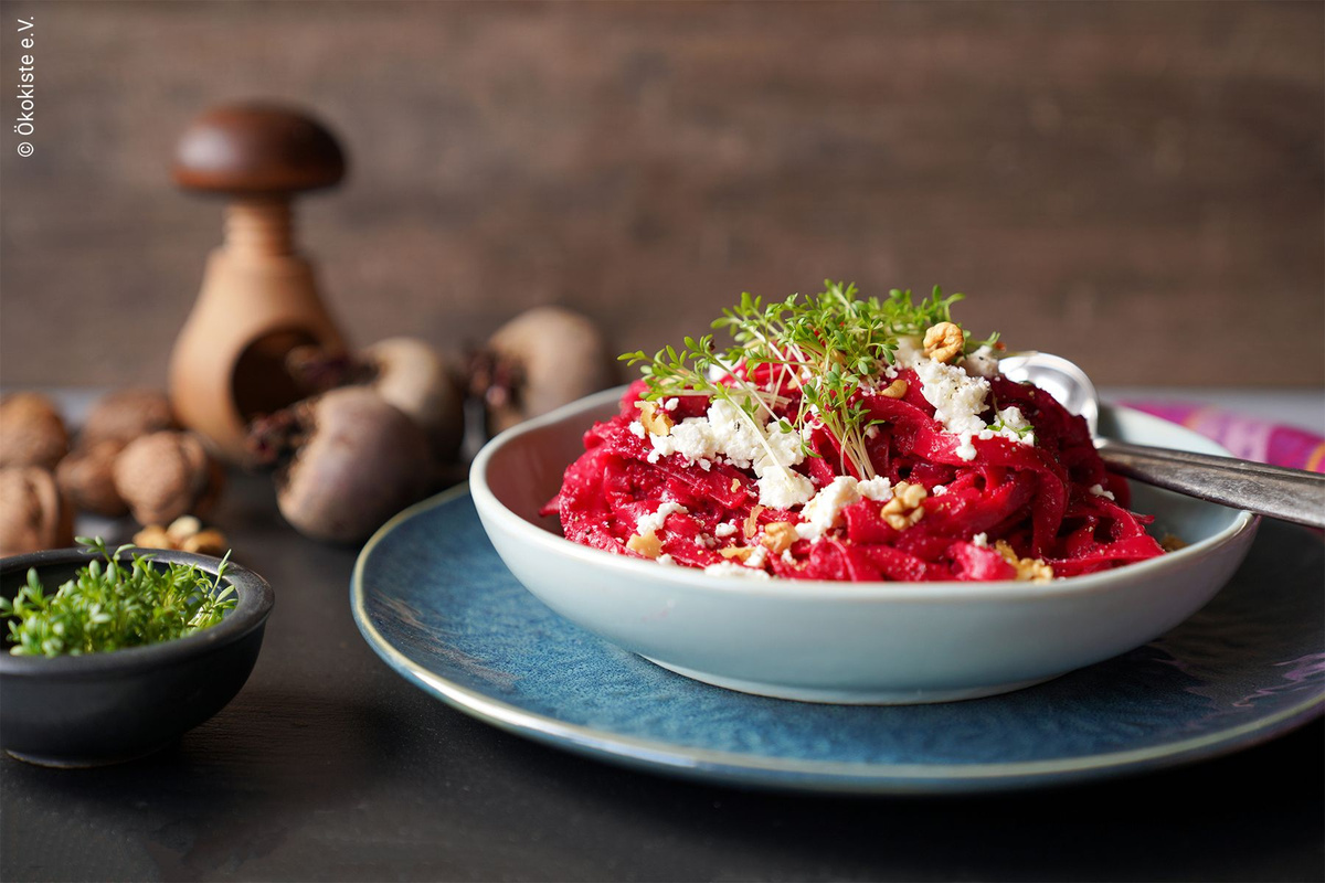 KI generiert: Das Bild zeigt eine Auswahl an Wurzelgemüsen, darunter lila Karotten, Pastinaken und eine Steckrübe, auf einem Holztisch arrangiert.
