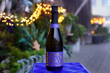 KI generiert: Das Bild zeigt eine Weinflasche mit der Aufschrift "Schönhals Samt & Seide" auf einer hölzernen Treppe, die von einem grauen Stoff umgeben ist. Der Fokus liegt auf der Weinflasche.