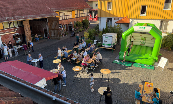 KI generiert: Ein Hof mit Menschen an Tischen, einer Hüpfburg und einem Stand.