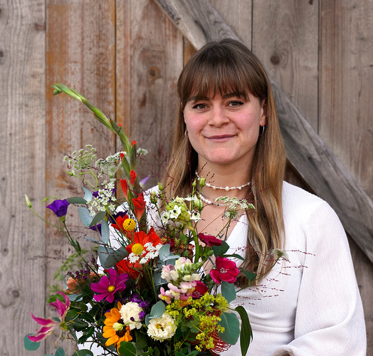 KI generiert: Frau in Weiß mit buntem Blumenstrauß vor Holzhintergrund.