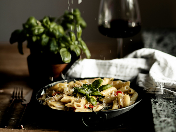 KI generiert: Ein Teller Pasta mit Basilikum, daneben ein Glas Rotwein und eine Basilikumpflanze.