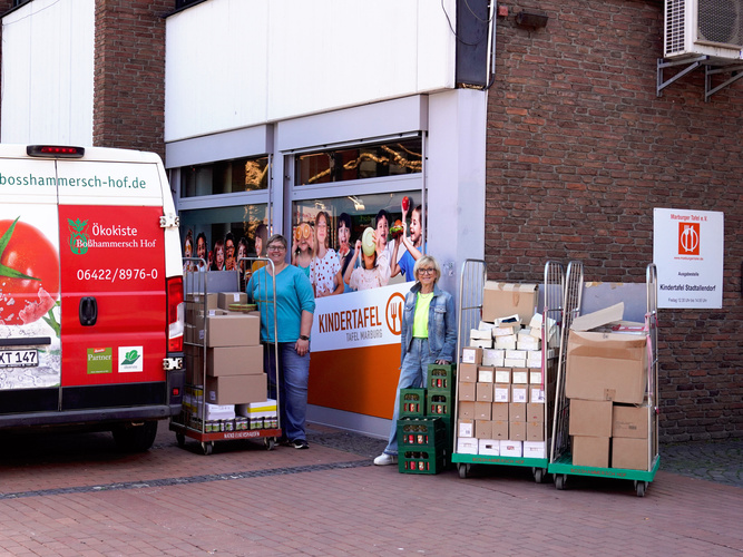 KI generiert: Ein Lieferwagen liefert Kisten zur Kindertafel Marburg. Text: "Ökokiste Bösshammer ..." "KINDERTA..."