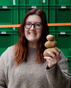 KI generiert: Eine Frau hält einen Wirsingkohl lächelnd vor einer Wand aus grünen Behältern. Der Hauptinhalt des Bildes ist die Präsentation des Kohls in einem fröhlichen Kontext.