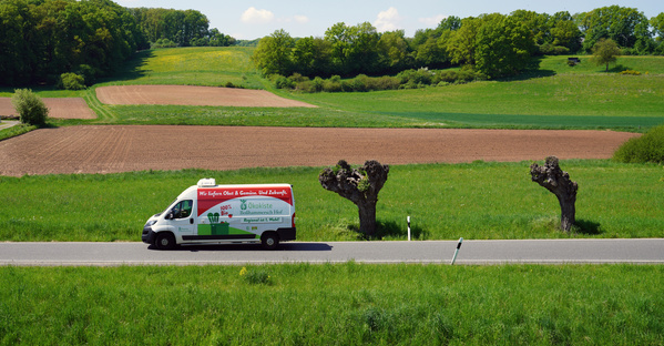 KI generiert: Ein Lieferwagen fährt auf einer Straße durch eine grüne Landschaft. Text: "Ökokiste".