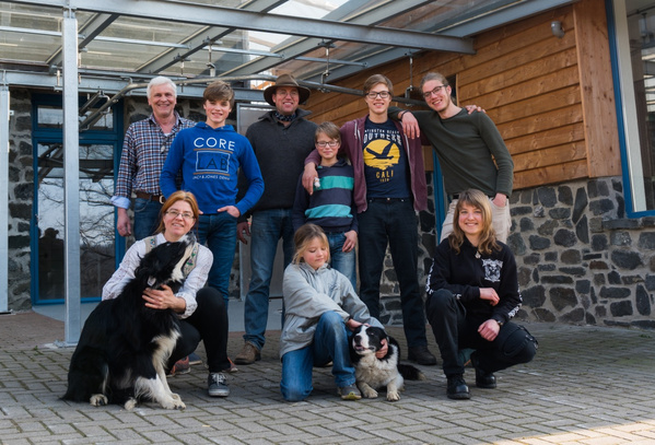 KI generiert: Eine Gruppe von Menschen posiert lächelnd vor einem Gebäude mit zwei Hunden.