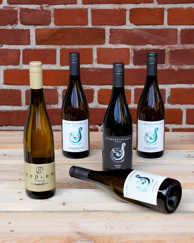 KI generiert: Fünf Weinflaschen vor einer Ziegelwand, teils liegend und stehend. Haupttext: "Schwarztrauber", "Keller".