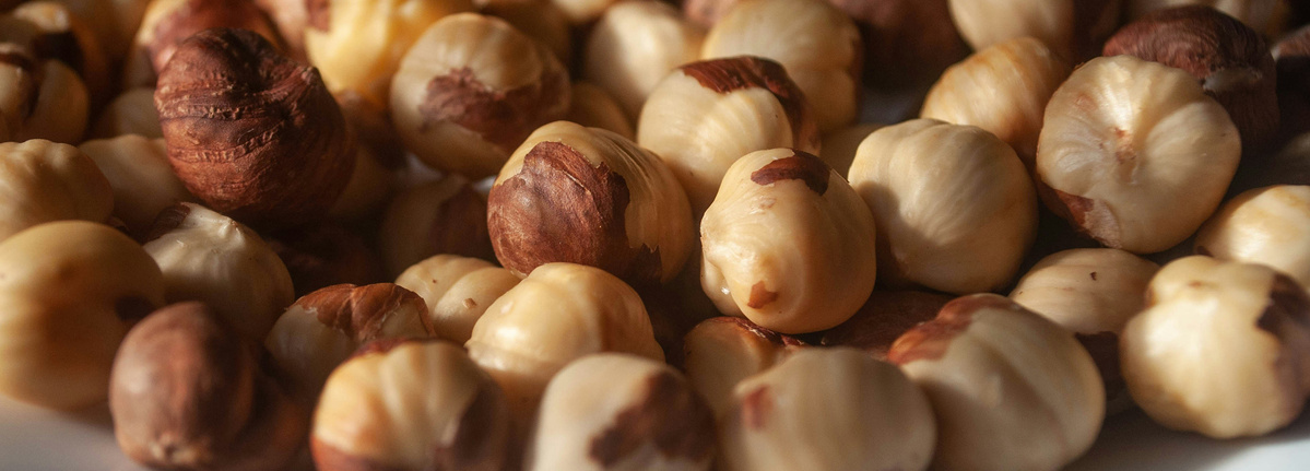 KI generiert: Das Bild zeigt eine Nahaufnahme von vielen geschälten Haselnüssen in verschiedenen Brauntönen. Der Fokus liegt auf der natürlichen Struktur und Farbe der Nüsse.