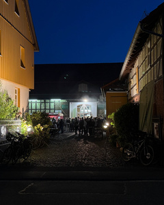 Das Bild zeigt mehrere Personen, die in einer Küche zusammenarbeiten, vermutlich bei einem Kochkurs oder einer Gruppenkochaktivität. Sie tragen Schürzen und sind mit der Zubereitung von Zutaten beschäftigt.