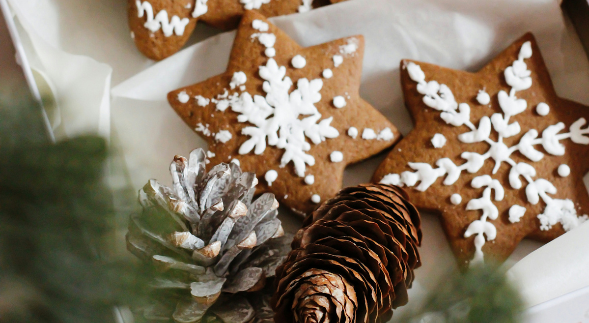 KI generiert: Das Bild zeigt weihnachtlich dekorierte Lebkuchenplätzchen in verschiedenen Formen, darunter ein Lebkuchenmann, ein Rentier und Schneeflocken. Neben den Plätzchen liegen Tannenzapfen, eingebettet in einer festlichen Szenerie.