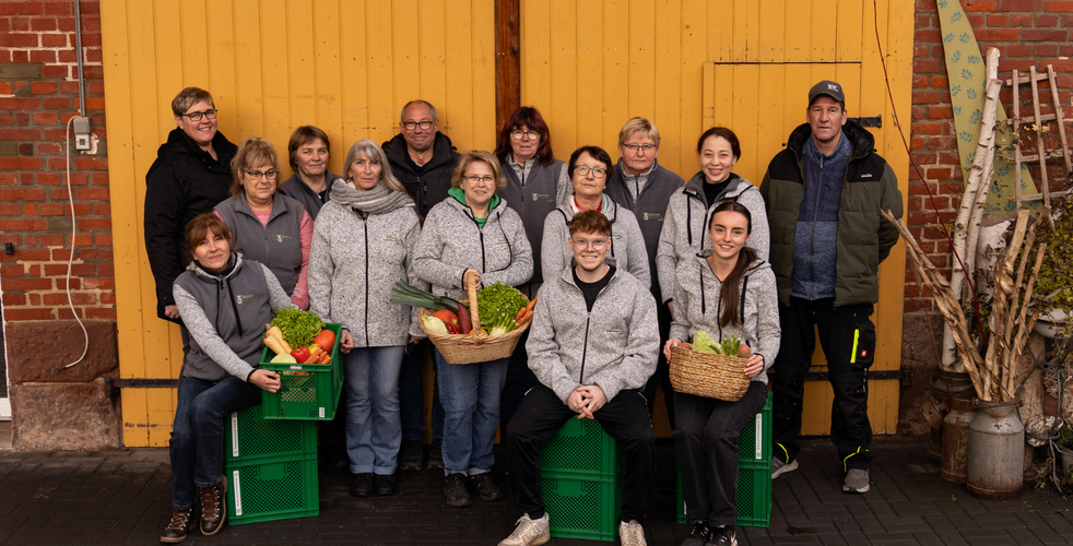 KI generiert: Gruppe von Leuten posiert mit Gemüsekörben, lächelt vor gelbem Tor.