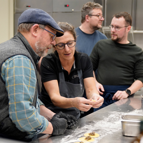 KI generiert: Mehrere Personen arbeiten gemeinsam in einer Küche an der Zubereitung von Teigtaschen.