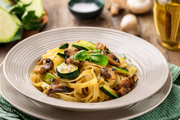 KI generiert: Ein Teller Pasta mit Zucchini, Pilzen und Basilikum, dekorativ angerichtet.