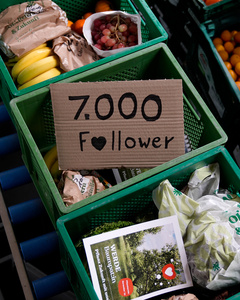 Das Bild zeigt mehrere Personen, die in einer Küche zusammenarbeiten, vermutlich bei einem Kochkurs oder einer Gruppenkochaktivität. Sie tragen Schürzen und sind mit der Zubereitung von Zutaten beschäftigt.