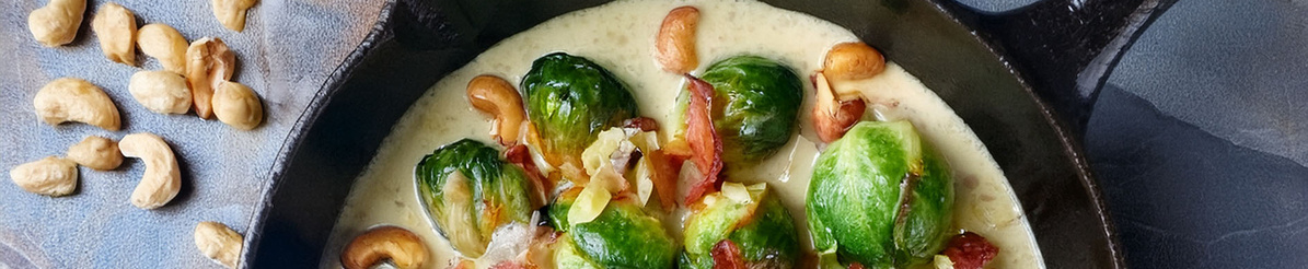 KI generiert: Rosenkohl in einer cremigen Sauce mit Cashewkernen in einer Pfanne, daneben liegen weitere Cashews auf einem Teller.
