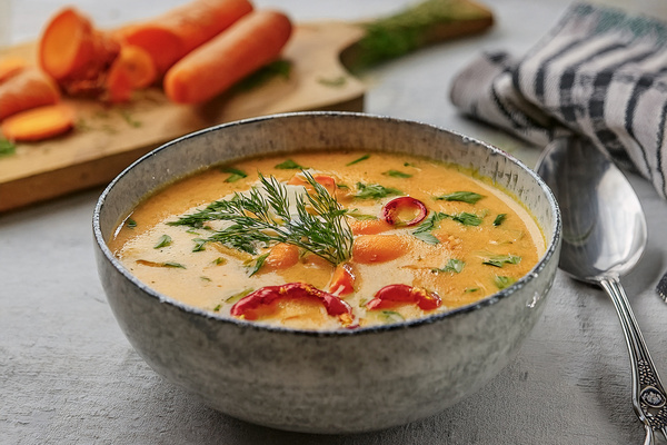 KI generiert: Eine Schüssel Gemüsesuppe mit Karotten und Kräutern auf einem Tisch.