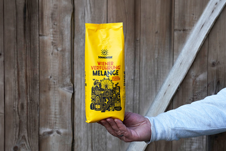 KI generiert: Das Bild zeigt eine Weinflasche mit der Aufschrift "Schönhals Samt & Seide" auf einer hölzernen Treppe, die von einem grauen Stoff umgeben ist. Der Fokus liegt auf der Weinflasche.