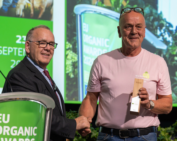 KI-generierte Beschreibung: Zwei Männer halten Weinflaschen und lächeln. Text: "23. September 2017 EUROPEAN ORGANIC DAYS".