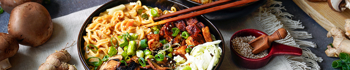 KI generiert: Eine Schüssel Ramen mit Gemüse und Holzstäbchen, umgeben von Pilzen und Gewürzen.