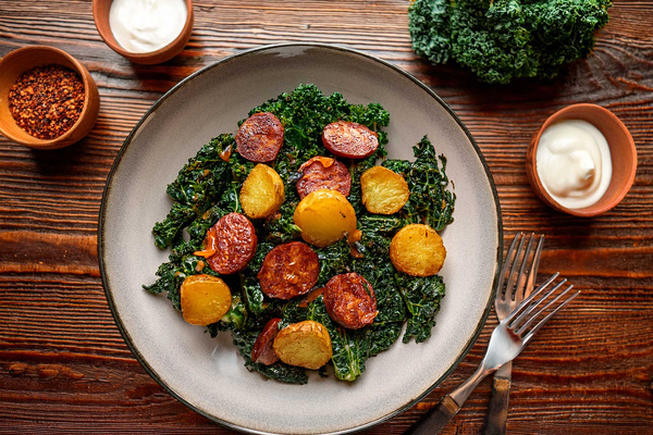 KI generiert: Ein Teller mit Grünkohl und gebratenen Kartoffelscheiben, umgeben von Gewürzen und Soße.