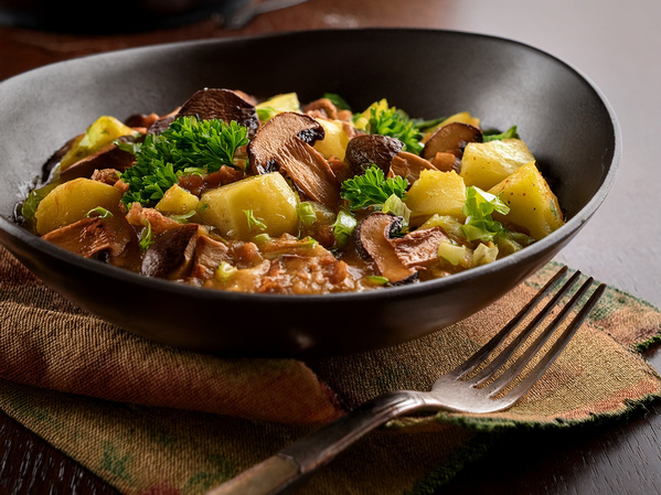 KI generiert: Ein Teller mit Pilz-Kartoffelgericht, garniert mit Petersilie, auf einem Tisch mit Gabel und Serviette.