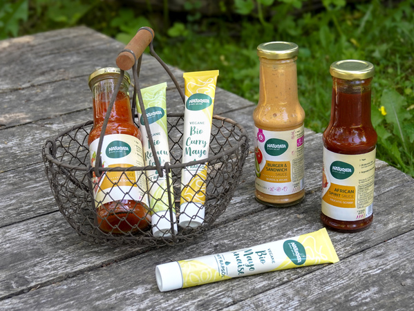 KI generiert: Verschiedene "Naturata"-Saucen und -Dips in einem Korb auf einem Holztisch im Freien.