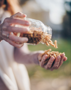 KI generiert: Das Bild zeigt eine Nahaufnahme von Händen, die Spiralnudeln aus einem Glas schütten. Die Szene trägt einen entspannten, natürlichen Charakter und ist im Freien aufgenommen.