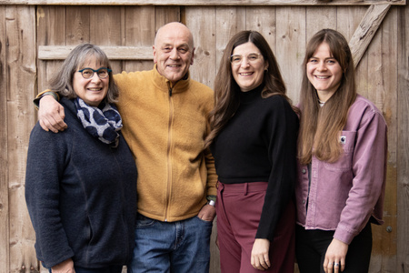 KI generiert: Das Bild zeigt vier Personen, die lächelnd vor einer Holzwand stehen. Die Menschen stehen nah beieinander und wirken fröhlich und verbunden.