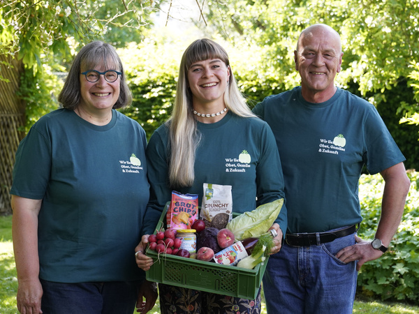 KI generiert: Drei Personen in grünen T-Shirts mit Obstkiste; Text: "Wir liefern Obst, Gemüse & Zukunft".