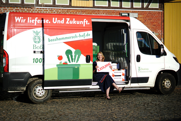 Susanne sitzt im Lieferwagen und hält Spendenscheck für Marburger Tafel