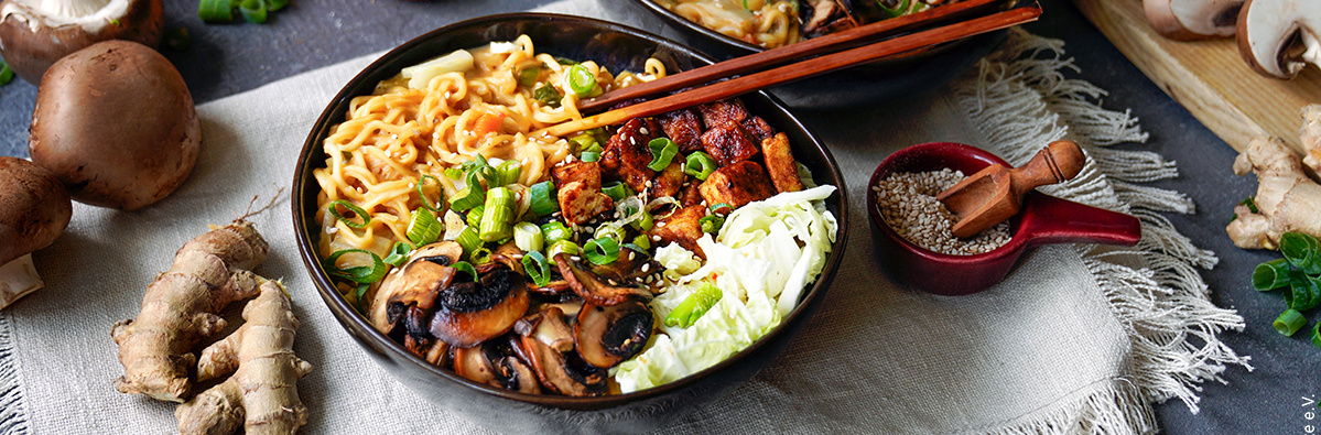 KI generiert: Schüssel mit Nudeln, Pilzen, Gemüse und Chopsticks, arrangiert auf einem dekorativen Tuch.