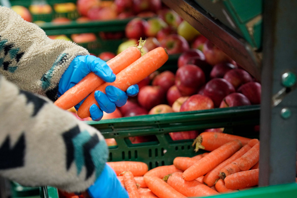 KI generiert: Eine Person hält Karotten vor einer Auslage mit Äpfeln.