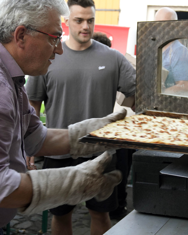 KI generiert: Ein Mann holt Flammkuchen aus einem Ofen.
