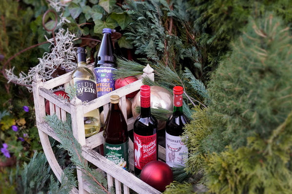 KI generiert: Eine Holzkiste mit Glühweinflaschen, dekoriert mit Tannenzweigen und Weihnachtskugeln. Text: "Glühwein".