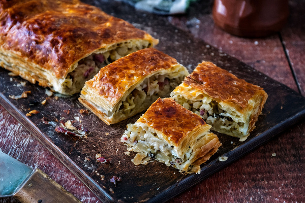 KI generiert: Das Bild zeigt ein Stück Apfelkuchen auf einem Teller, daneben liegt eine Gabel. Der Fokus liegt auf der knusprigen Kruste und der saftigen Füllung des Kuchens.