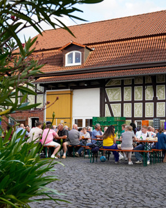 Das Bild zeigt mehrere Personen, die in einer Küche zusammenarbeiten, vermutlich bei einem Kochkurs oder einer Gruppenkochaktivität. Sie tragen Schürzen und sind mit der Zubereitung von Zutaten beschäftigt.