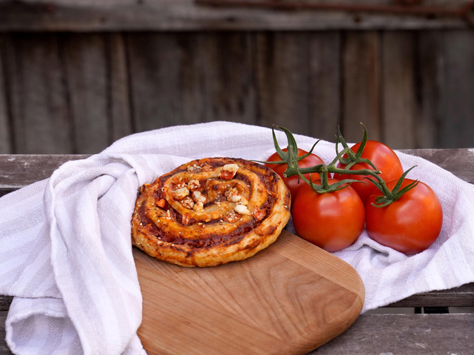 KI generiert: Blätterteiggebäck und Tomaten auf Holzbrett mit Stofftuch, rustikaler Hintergrund.