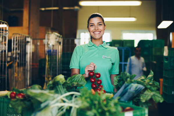 Ein Ökokisten-Fahrer mit Migrationshintergrund überreicht eine Ökokiste an eine Firma in der Region.