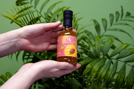 KI generiert: Das Bild zeigt eine Weinflasche mit der Aufschrift "Schönhals Samt & Seide" auf einer hölzernen Treppe, die von einem grauen Stoff umgeben ist. Der Fokus liegt auf der Weinflasche.