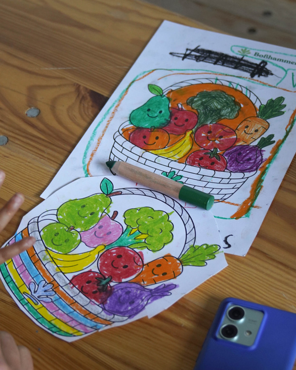 KI generiert: Zwei bunte Zeichnungen von Obst und Gemüse in einem Korb, mit Kinderhand und Buntstift. Text: "Boßhammer Hof".